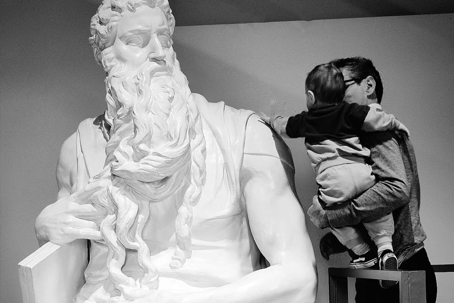 An adult is holding a child in their arms to let them touch the copy of Michelangelo's Moses.