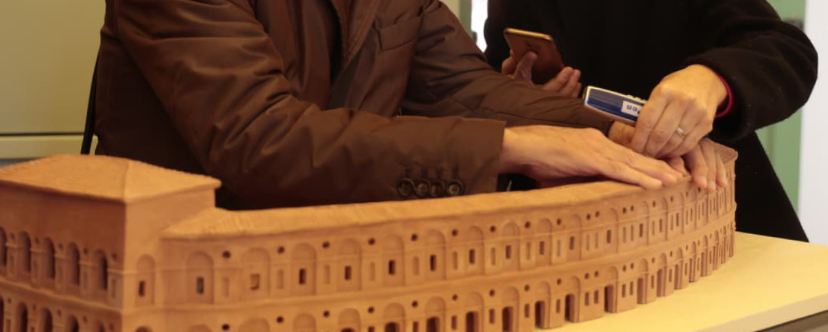 Due persone toccano con le mani un modellino dello sferisterio di Macerata. Una delle due persone tiene in mano un'audiopen.