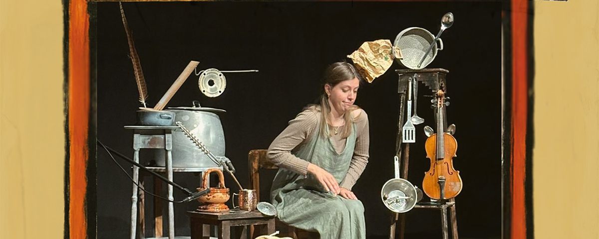 «Una giovane donna seduta su una sedia di legno al centro di una scena teatrale. Attorno a lei sono disposti oggetti di uso domestico trasformati in strumenti: pentole, coperchi, un mestolo, un colino, una teiera, un violino appeso a uno sgabello alto e altri utensili metallici che creano un’atmosfera creativa e artigianale. Lo sfondo è scuro, la luce è concentrata sulla protagonista.»