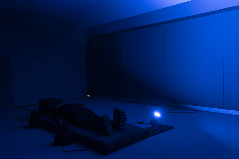 The Silent World di Rachele Maistrello: un ambiente immerso in luce blu, una persona distesa su una pedana e una piccola luce direzionale.