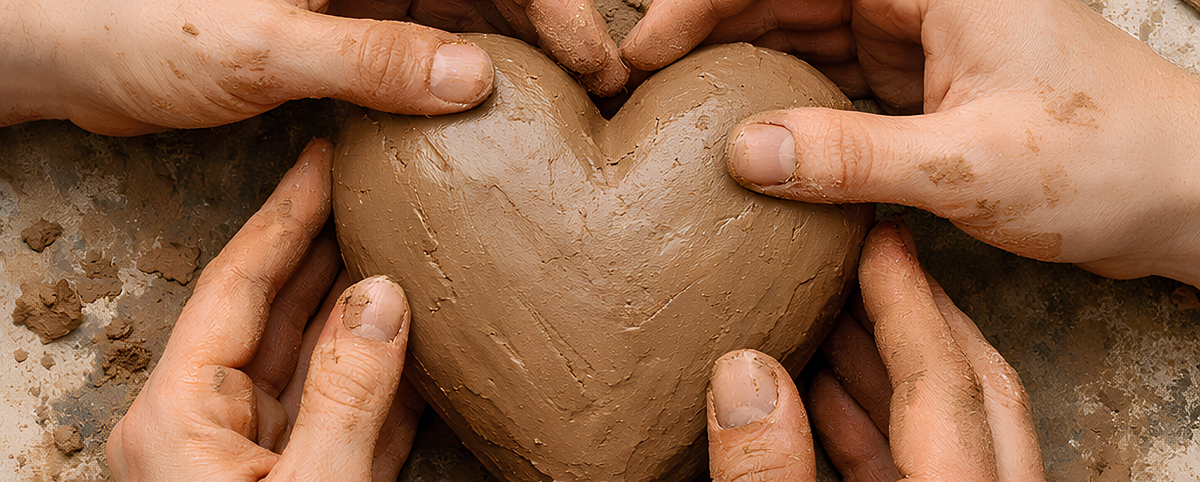 Mani di più persone, sporche di argilla, modellano insieme un grande cuore di creta.